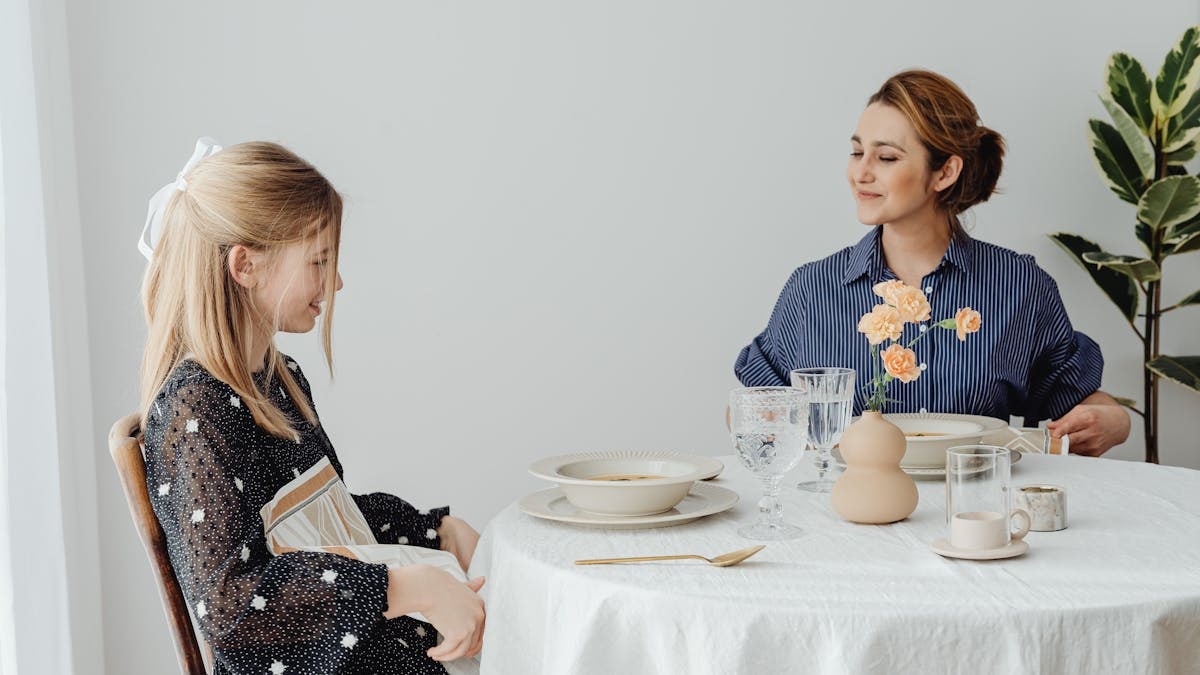 Mother and daughter sharing a happy meal together in a minimalistic dining room setting.